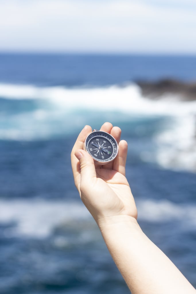 Hand holding a compass in front of the ocean